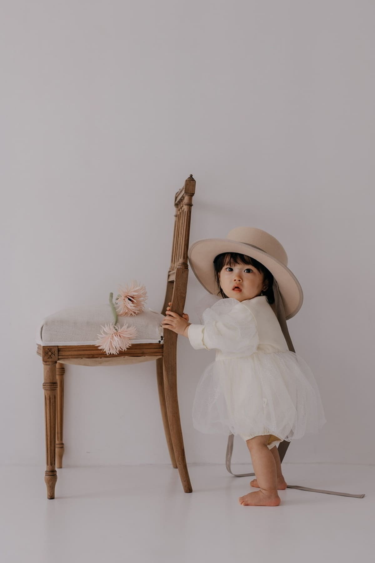 帽子をかぶった小さい子どもが椅子を持って立っている写真