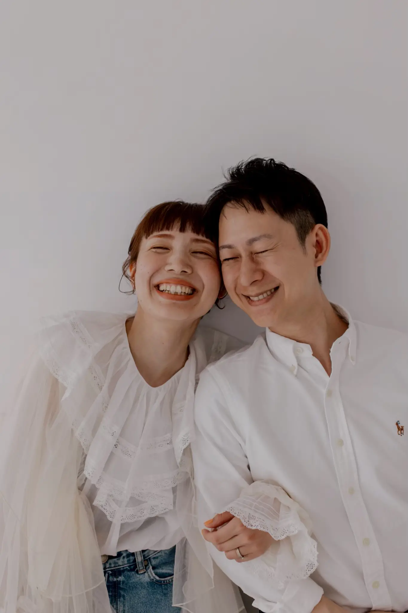 白い服のカップルが頬を寄せ合って笑う記念日写真