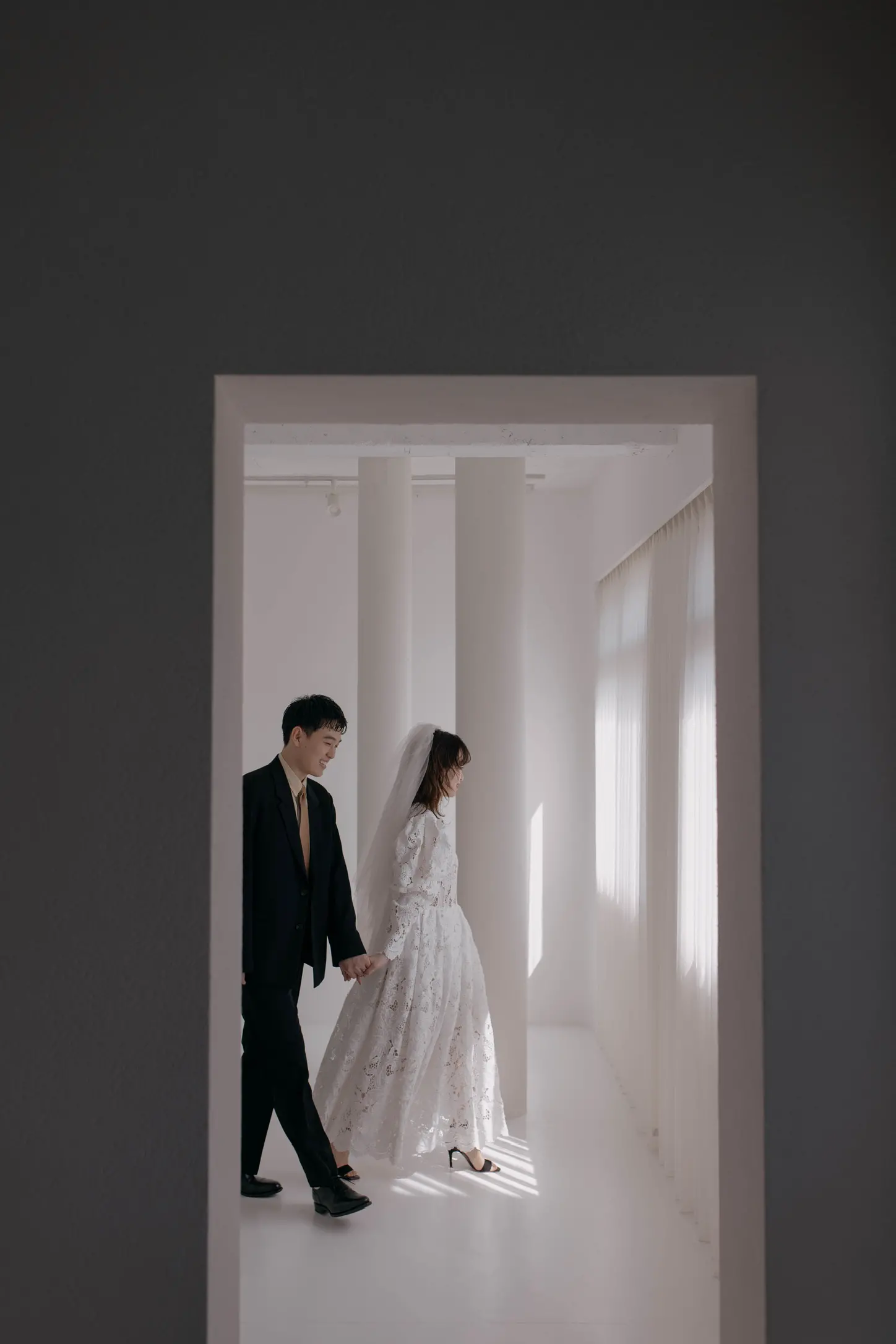 ウェディングドレス姿の花嫁と紋付スーツの新郎が白いスタジオを歩く写真