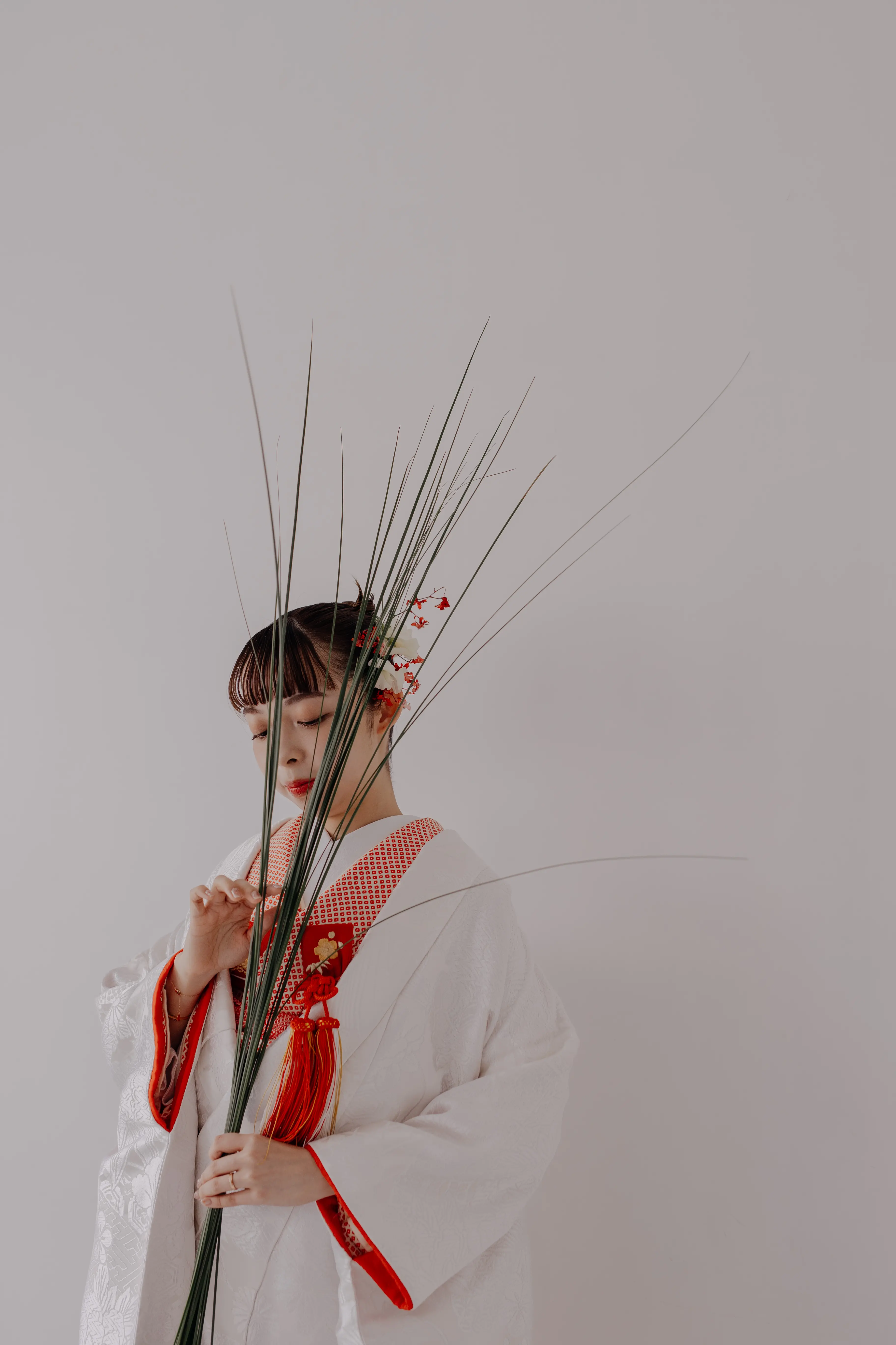 赤い帯の白無垢姿の花嫁が植物のオブジェを抱える写真