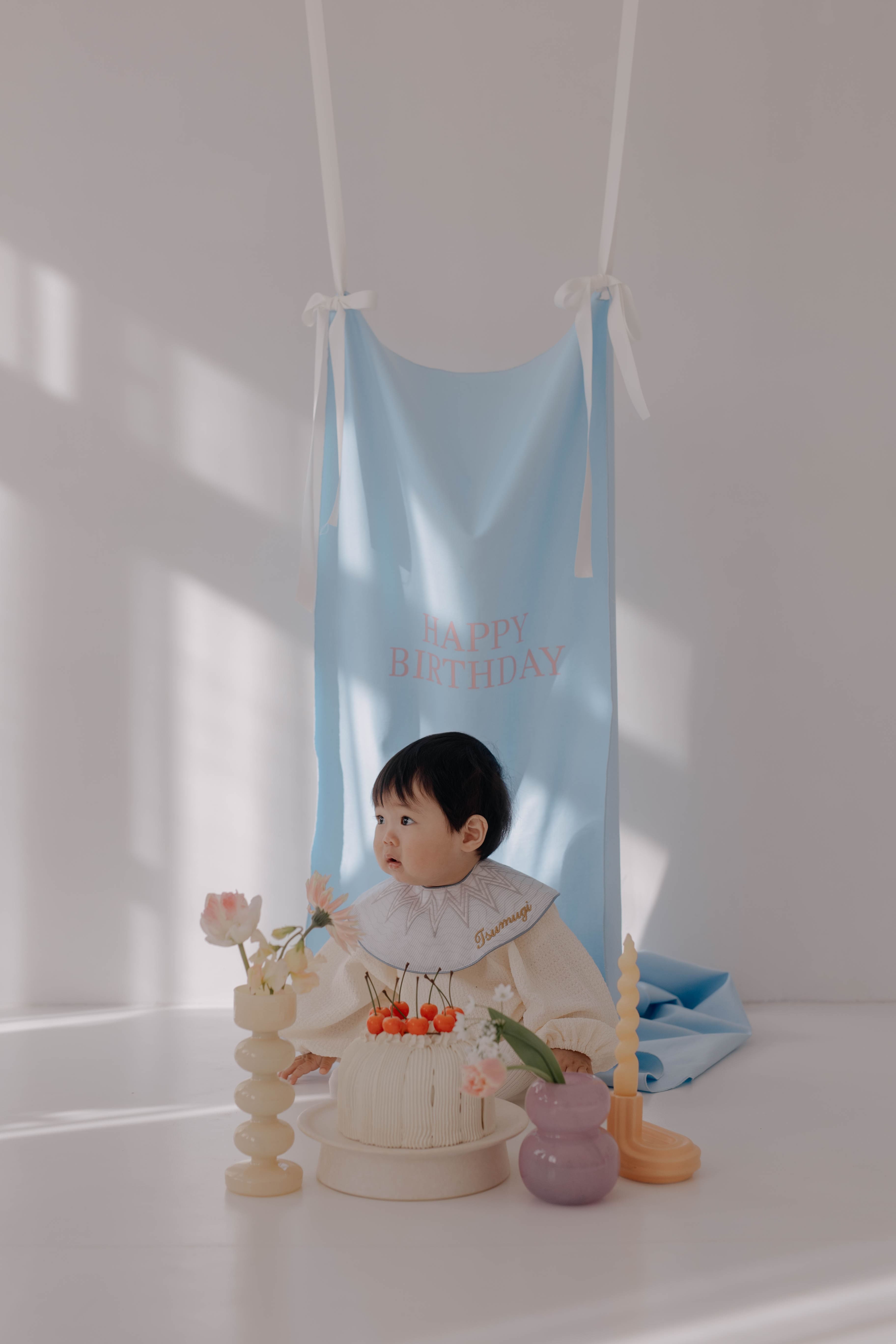 HAPPYBIRTHDAYタペストリーの前でクレイケーキを前に座る赤ちゃんの誕生日撮影