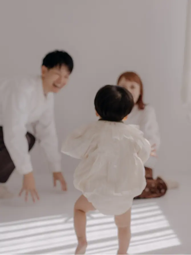 両親に向かってよちよち歩きする赤ちゃんの家族写真