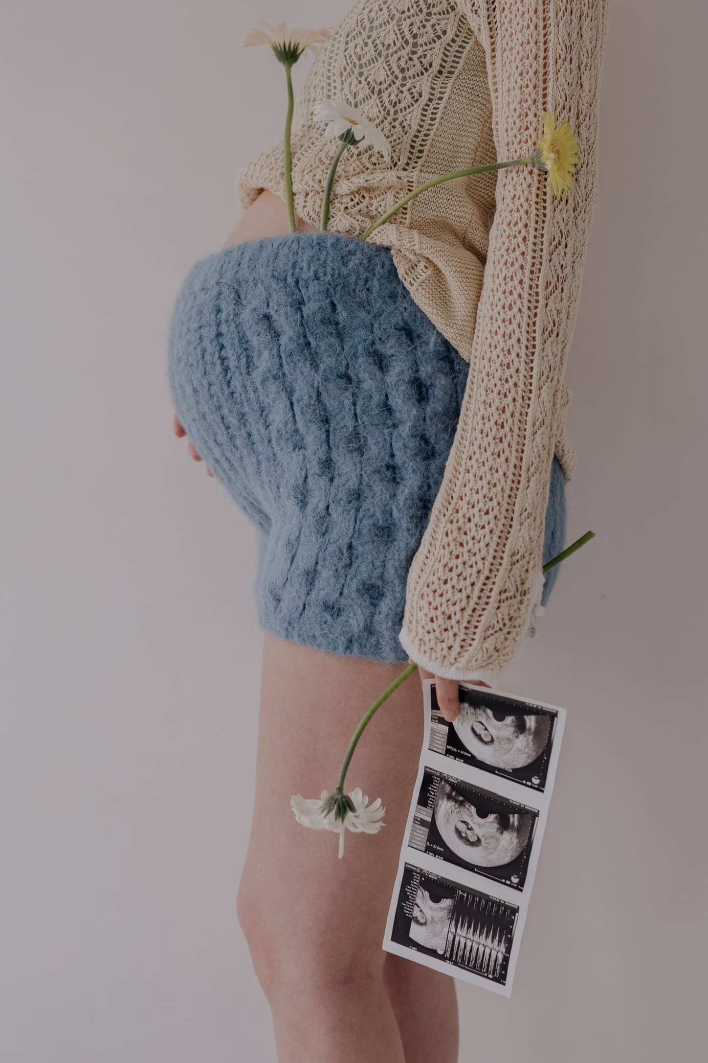 妊婦さんが花とエコー写真を手に持ち横からお腹を見せるマタニティフォト
