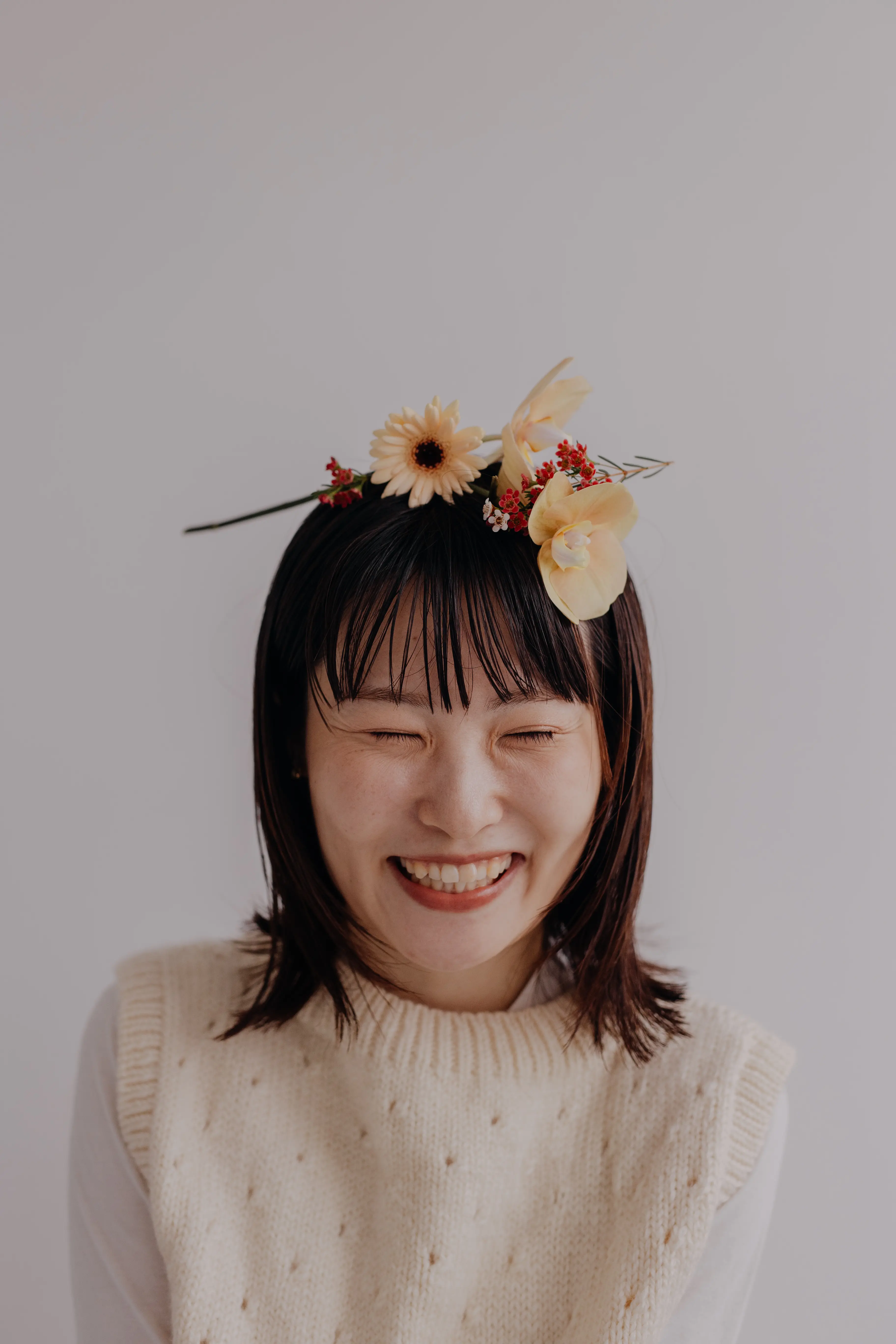 花のボケを前景に白いニットの女性が立つプロフィール写真