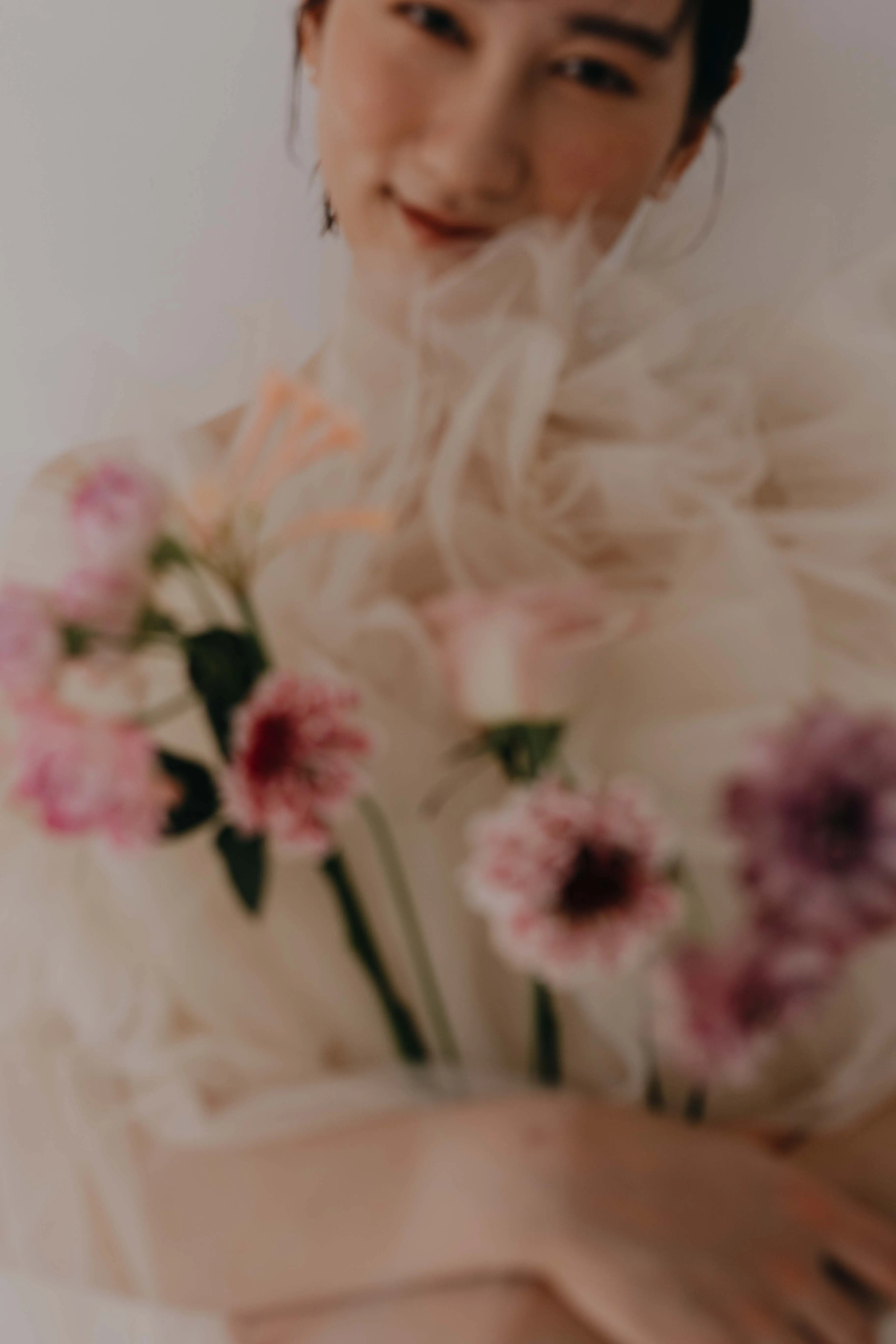 白いチュールのトップスを着た女性がピンクと紫の花束を抱えているやわらかな雰囲気のポートレート