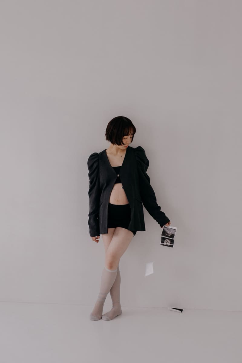 黒いパフスリーブジャケットを羽織りエコー写真を手に持ちながら下を向いて立つ妊婦のマタニティフォト