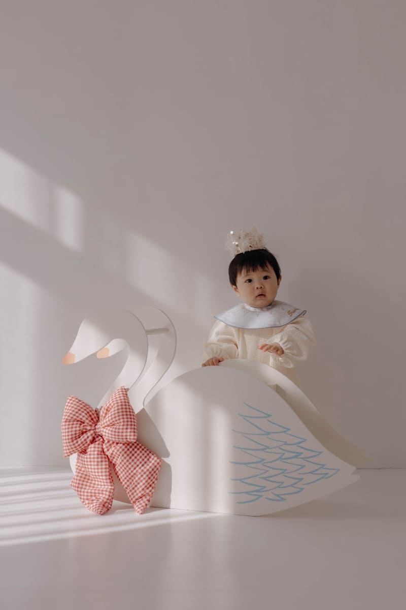 小さなティアラをつけた赤ちゃんが白鳥のオブジェの横に座り、こちらを見つめるポートレート
